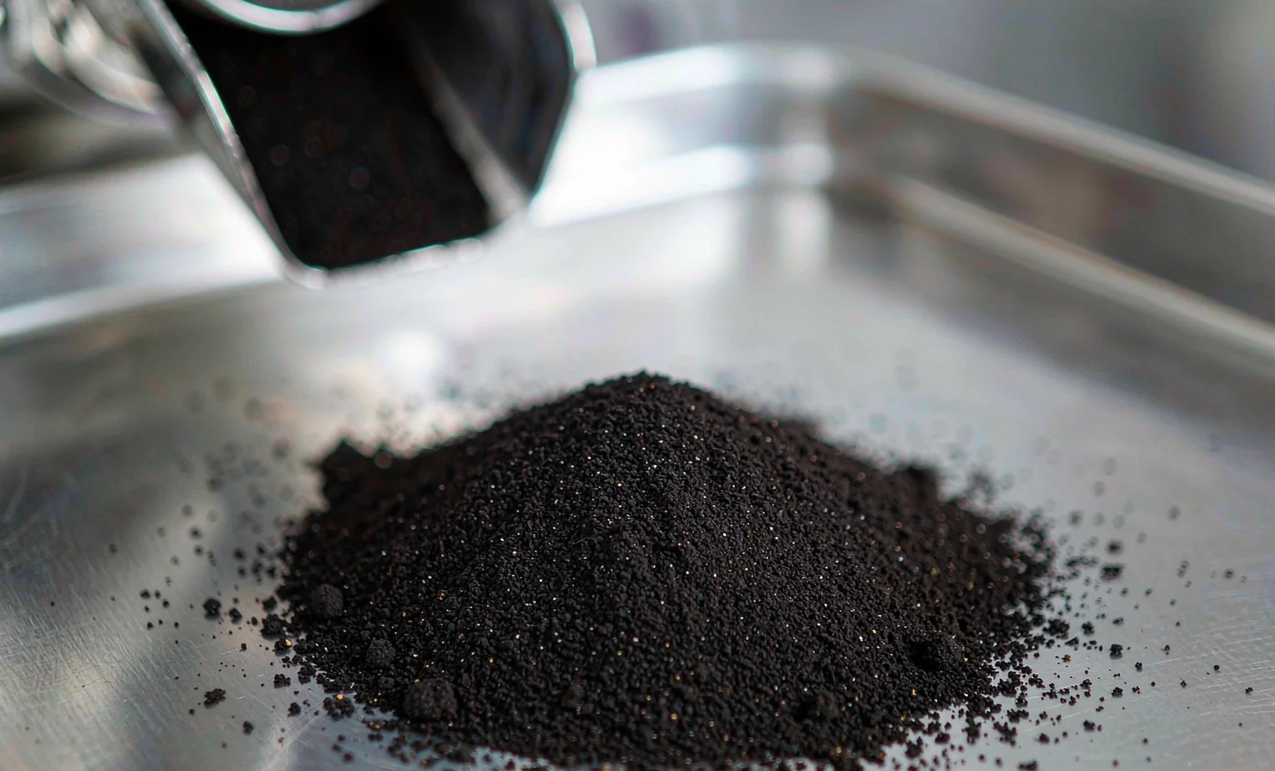 Freshly milled fine black pepper powder on a stainless steel tray at a grinder discharge outlet